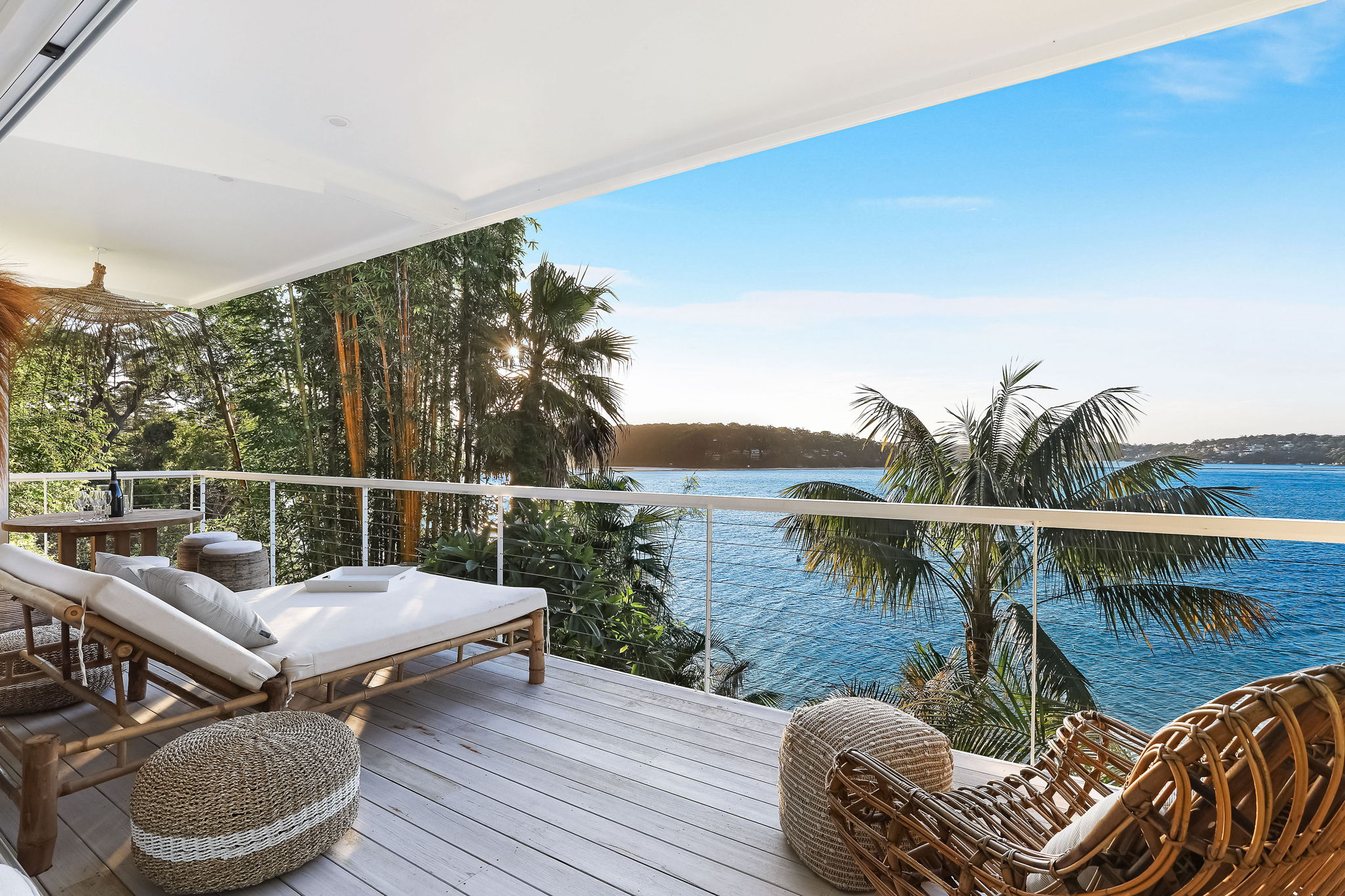 Bundeena Sands waterfront deck with lounge beds, rattan seating, palm trees and ocean bay views